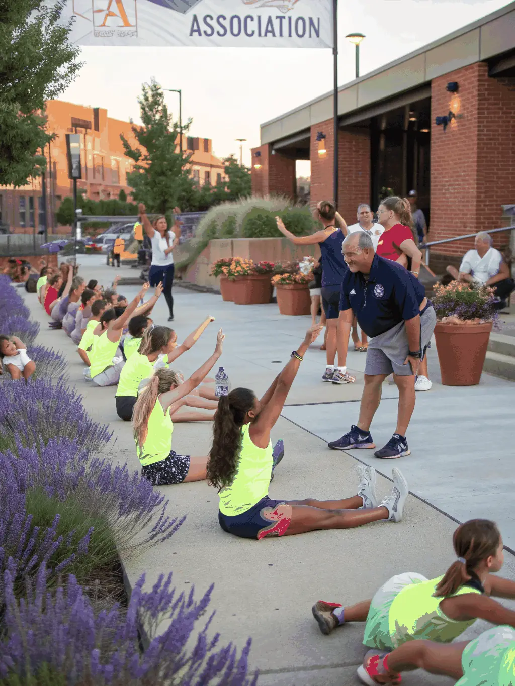 A diverse group of people participating in a community gymnastics event outdoors, with music and a festive atmosphere. The event promotes inclusivity and community bonding.
